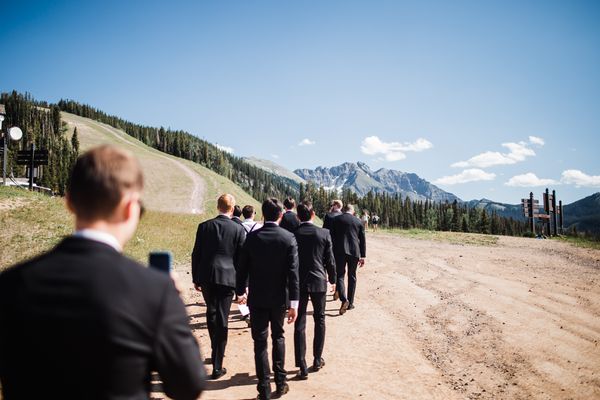 Guests in dark suits walking across open ground toward San Sophia Overlook with the mountains ahead