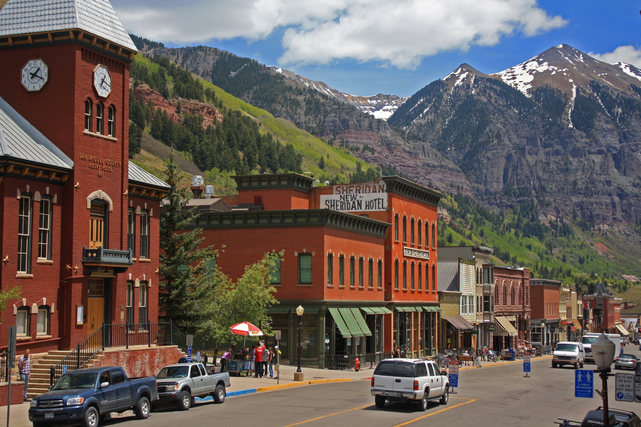 Historic red brick buildings and the San Miguel County Courthouse on a downtown Telluride street, with snow-capped peaks beyond