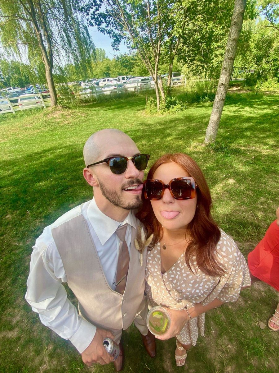 Kyle and Karli in sunglasses at an outdoor event, playfully sticking out their tongues