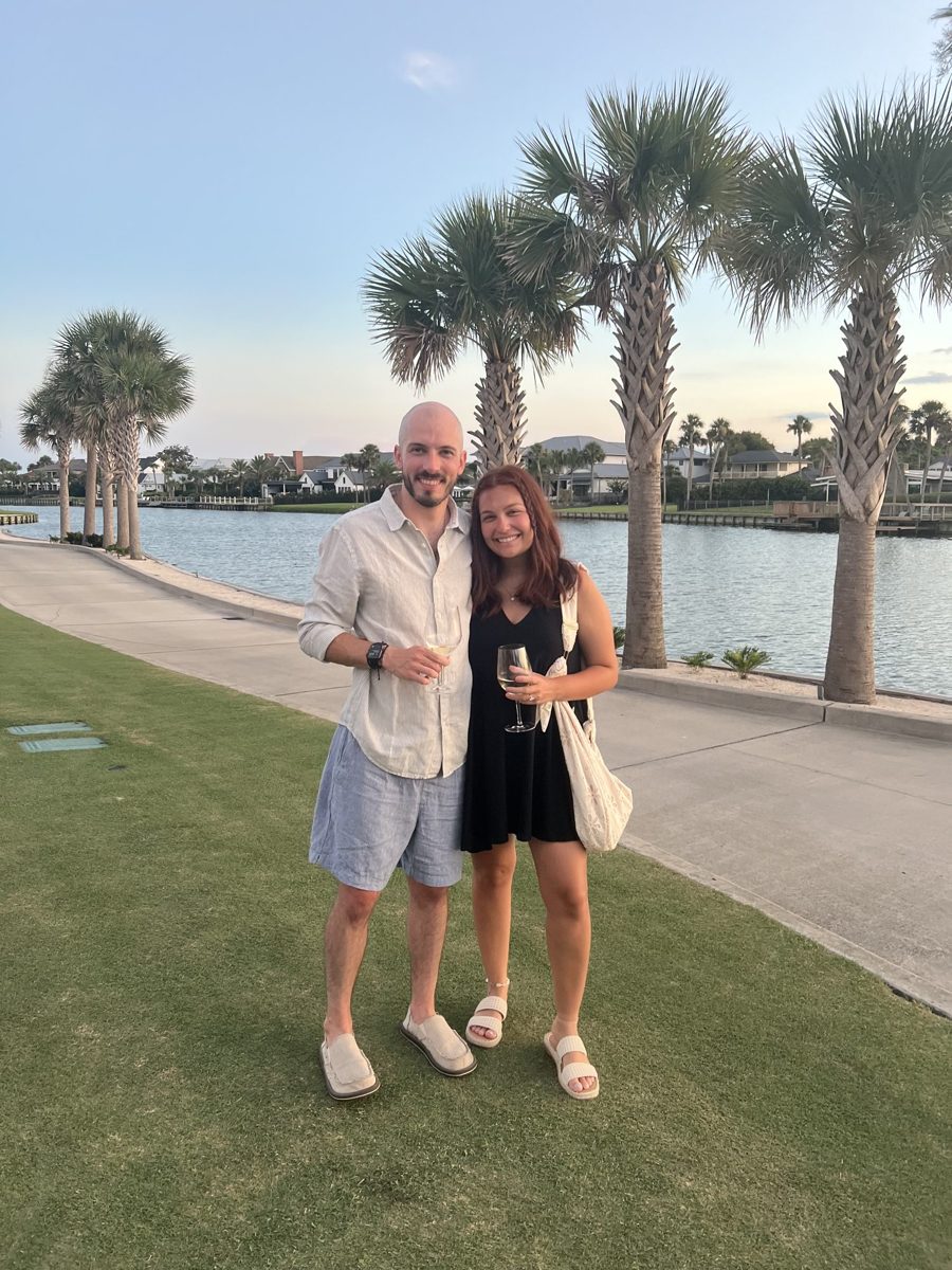 Kyle and Karli standing together on a waterfront path lined with palm trees