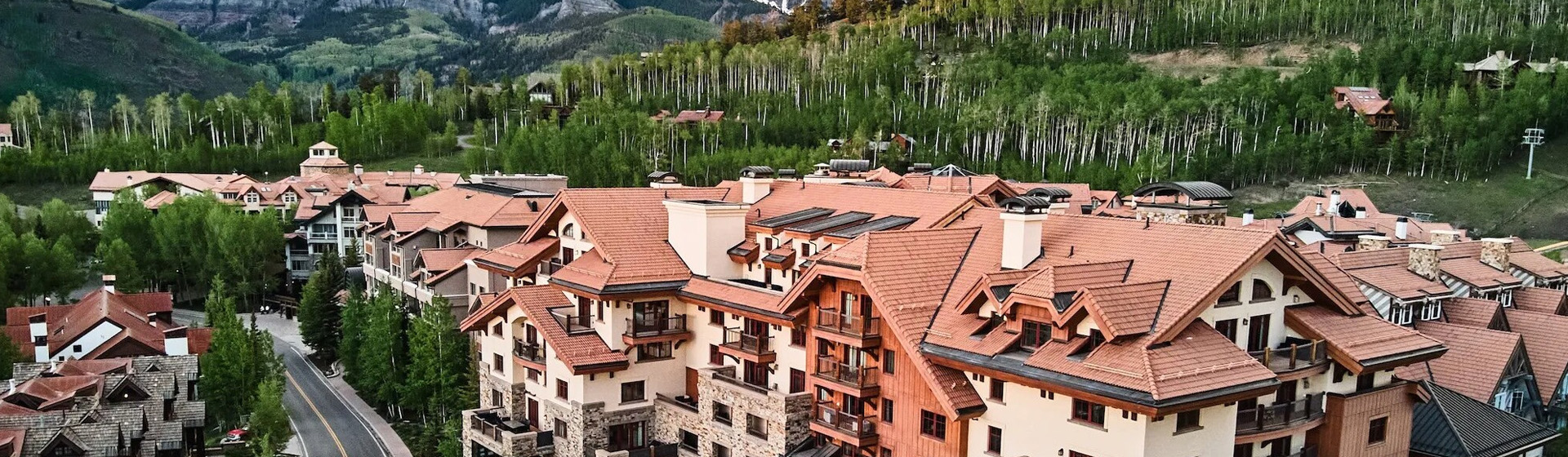 Terra-cotta rooftops of Mountain Village hotels with aspen-covered mountains behind