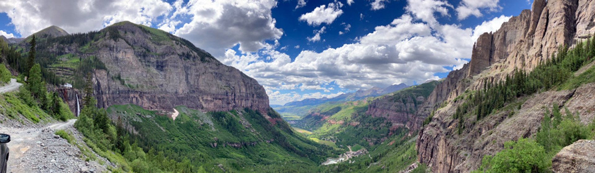 Panoramic view down a green Telluride valley between red rock cliffs, under a blue sky with clouds