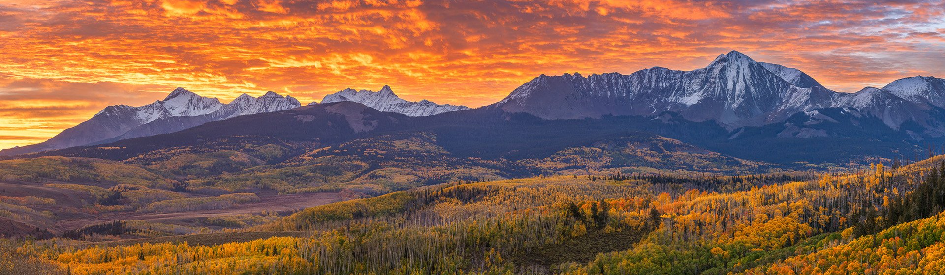 Snow-capped San Juan peaks under a fiery orange sunrise above golden aspen forests